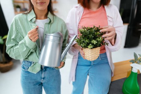 Téléchargez les photos : Jeunes femmes avec un arrosoir et une plante d'intérieur dans un pot - en image libre de droit