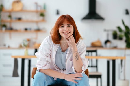 Photo for Portrait of a beautiful woman sitting on a chair in a modern kitchen on the background - Royalty Free Image
