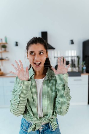 Photo for Young woman shows her hands in flour in the kitchen to the camera - Royalty Free Image