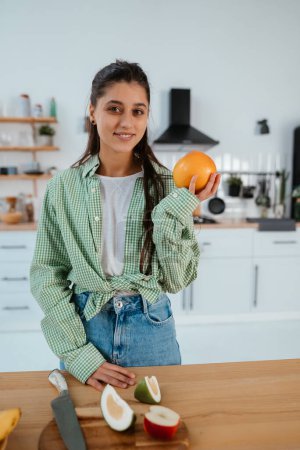 Photo for Happy healthy woman cutting fruits on a wooden board while making breakfast in a kitchen - Royalty Free Image