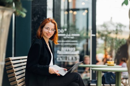 Téléchargez les photos : Belle rousse femme travaillant sur ordinateur portable au café en plein air - en image libre de droit