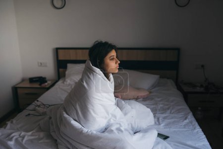 Foto de Mujer joven envuelta en una manta mirando a la distancia en la habitación del hotel - Imagen libre de derechos