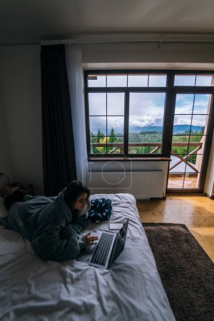 Téléchargez les photos : Femme travaillant sur un ordinateur portable tout en étant couché sur le lit - en image libre de droit