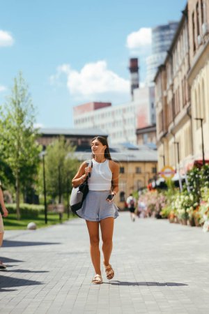 Téléchargez les photos : Urban young hipster woman with stylish backpack walks around the city near a building in the spring day. Pretty girl travels. - en image libre de droit