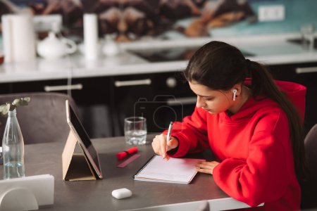Foto de Hermosa chica con auriculares está sosteniendo un bolígrafo en su mano y escribir información de la tableta a un cuaderno. Foto de alta calidad - Imagen libre de derechos