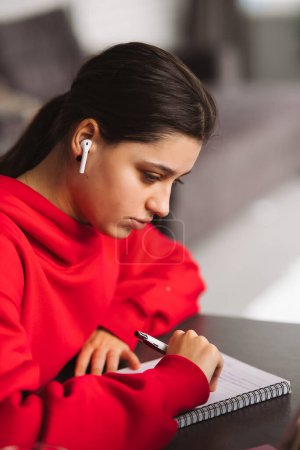 Téléchargez les photos : Femme avec casque tient un stylo dans sa main et d'écrire des informations de tablette à un ordinateur portable. Photo de haute qualité - en image libre de droit