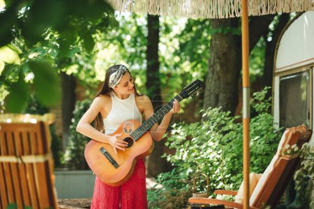 Foto de Chica hippie feliz está teniendo un buen rato con tocar en la guitarra en caravana remolque. Vacaciones, vacaciones, concepto de viaje.Foto de alta calidad - Imagen libre de derechos