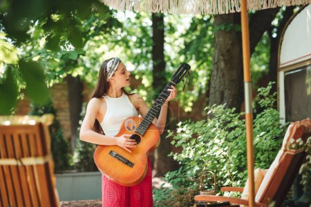 Photo for Happy hippie girl is having a good time with playing on guitar in camper trailer. Holiday, vacation, trip concept.High quality photo - Royalty Free Image