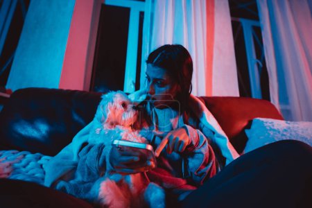 Photo for Beautiful young girl at home in a dark room playing with her dog and sits in front of a monitor or TV. High quality photo - Royalty Free Image