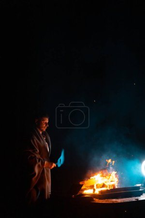 Téléchargez les photos : Homme préparant barbecue grill à cuire sur le feu. Tir à l'extérieur. Geler le moment du feu. Photo de haute qualité - en image libre de droit