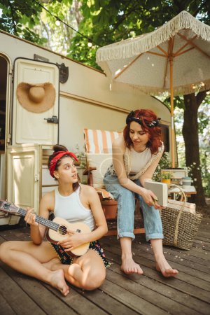 Foto de Chicas hippies felices están teniendo un buen rato con tocar en la guitarra en caravana remolque. Vacaciones, vacaciones, concepto de viaje.Foto de alta calidad - Imagen libre de derechos