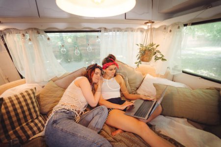 Foto de Chicas hippies felices están teniendo un buen rato juntos viendo la película en el ordenador portátil en un remolque campista. Vacaciones, vacaciones, concepto de viaje. Foto de alta calidad - Imagen libre de derechos