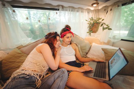 Foto de Chicas hippies felices están teniendo un buen rato juntos viendo la película en el ordenador portátil en un remolque campista. Vacaciones, vacaciones, concepto de viaje. Foto de alta calidad - Imagen libre de derechos