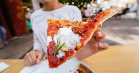 Photo for Womans hand holding a slice of pizza outdoor on terrace. - Royalty Free Image