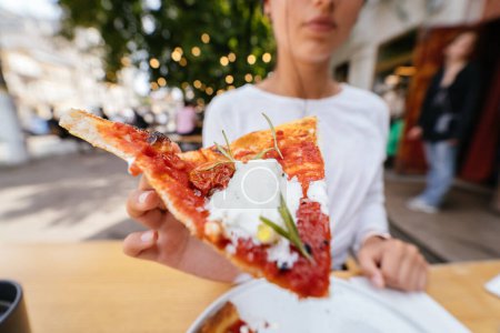 Téléchargez les photos : Femme main tenant une tranche de pizza en plein air sur la terrasse. - en image libre de droit