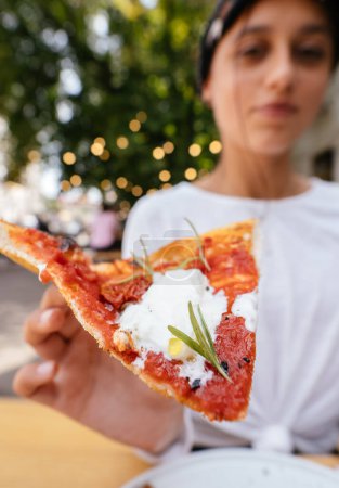 Photo for Womans hand holding a slice of pizza outdoor on terrace. - Royalty Free Image
