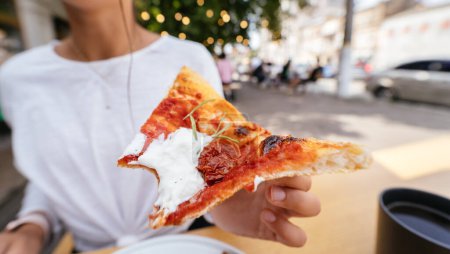 Photo for Womans hand holding a slice of pizza outdoor on terrace. High quality photo - Royalty Free Image