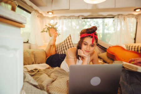 Photo for Portrait of a cute lesbian couple. Two girls spend time tenderly together watching movie on laptop in a camper trailer with LGBT flag on the wall. Love and attitude. LGBT concept. High quality photo - Royalty Free Image