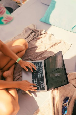 Foto de Hermosa chica en bikini está escribiendo en un ordenador portátil y tomar el sol en la playa. Foto de alta calidad - Imagen libre de derechos