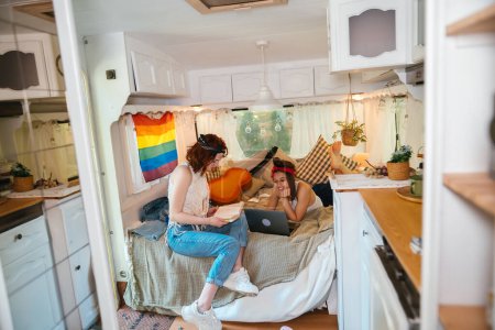 Téléchargez les photos : Portrait d'un couple lesbien mignon. Deux filles passent du temps ensemble à regarder des films sur ordinateur portable dans une caravane avec un drapeau LGBT sur le mur. Amour et attitude. Concept LGBT. Photo de haute qualité - en image libre de droit