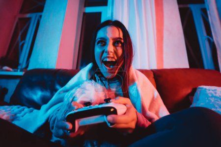 Photo for Close up portrait of A gamer or a streamer girl at home in a dark room with a game controller playing with her dog and sits in front of a monitor or TV. High quality photo - Royalty Free Image