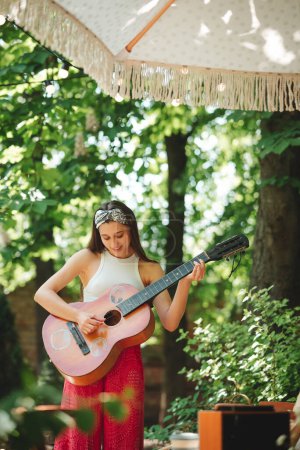 Happy hippie girl is having a good time with playing on guitar in camper trailer. Holiday, vacation, trip concept.High quality photo