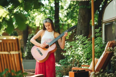 Photo for Happy hippie girl is having a good time with playing on guitar in camper trailer. Holiday, vacation, trip concept.High quality photo - Royalty Free Image