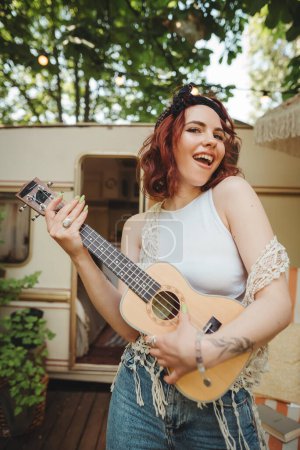 Photo for Happy hippie girl are having a good time with playing on guitar in camper trailer. Holiday, vacation, trip concept.High quality photo - Royalty Free Image