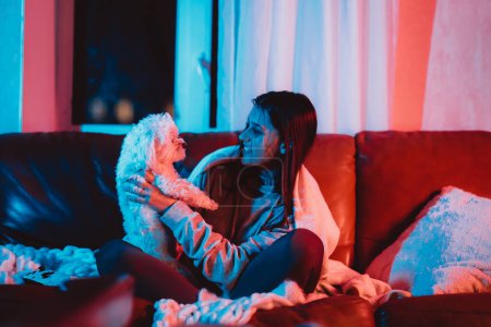 Photo for Beautiful young girl watching movie at home in a dark room with a popcorn bucket and playing with her dog and sits in front of a monitor or TV watching movie. Crazy emotions. High quality photo - Royalty Free Image