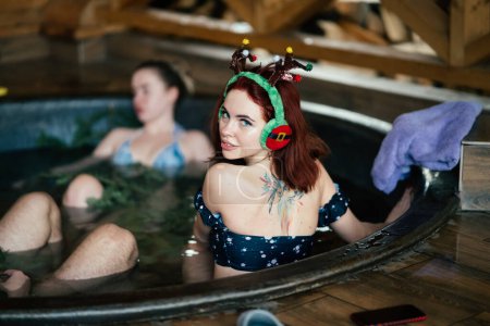 Photo for Young girls in bikinis bathing in an outdoor bathtub on winter holidays. Wooden cottage. High quality photo - Royalty Free Image