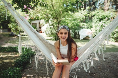 Téléchargez les photos : Joyeux hippie fille lit un livre dans hamac avoir un bon moment avec jouer dans caravane camping-car. Vacances, vacances, concept de voyage. Photo de haute qualité - en image libre de droit