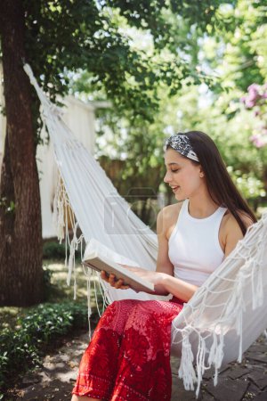 Foto de Chica hippie feliz está leyendo un libro en hamaca tener un buen rato con jugar en caravana remolque. Vacaciones, vacaciones, concepto de viaje.Foto de alta calidad - Imagen libre de derechos