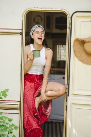 Happy hippie girl are having a good time with cup of tea in camper trailer. Holiday, vacation, trip concept.High quality photo