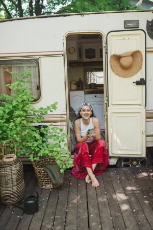 Téléchargez les photos : Bonne fille hippie passent un bon moment avec une tasse de thé dans la caravane camping-car. Vacances, vacances, concept de voyage. Photo de haute qualité - en image libre de droit