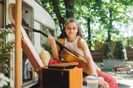 Téléchargez les photos : Bonne fille hippie passent un bon moment avec jouer à la guitare dans la bande-annonce du camping-car. Vacances, vacances, concept de voyage. Photo de haute qualité - en image libre de droit