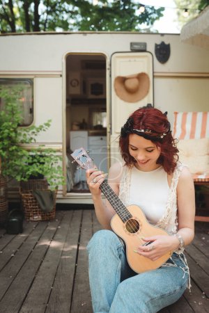 Photo for Happy hippie girl are having a good time with playing on guitar in camper trailer. Holiday, vacation, trip concept.High quality photo - Royalty Free Image