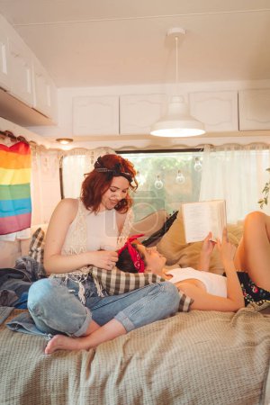 Foto de Retrato de una linda pareja de lesbianas. Dos chicas pasan tiempo juntas tiernamente en un remolque de caravana con bandera LGBT en la pared. Amor y actitud. Concepto LGBT. Foto de alta calidad - Imagen libre de derechos