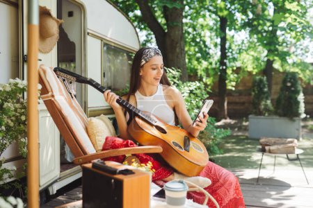 Foto de Chica hippie feliz están teniendo un buen rato con tocar en la guitarra en caravana remolque. Vacaciones, vacaciones, concepto de viaje.Foto de alta calidad - Imagen libre de derechos