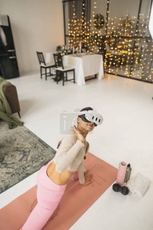 Téléchargez les photos : Exercices d'étirement des bras pendant les entraînements à domicile avec un casque de réalité virtuelle au milieu des célébrations de Noël. Photo de haute qualité - en image libre de droit