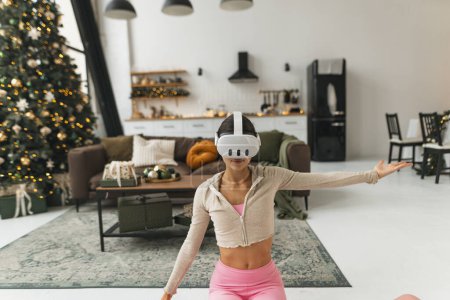 Foto de Absorto en la práctica de yoga, un entusiasta del fitness usa gafas de realidad virtual junto a un árbol de Navidad. Foto de alta calidad - Imagen libre de derechos