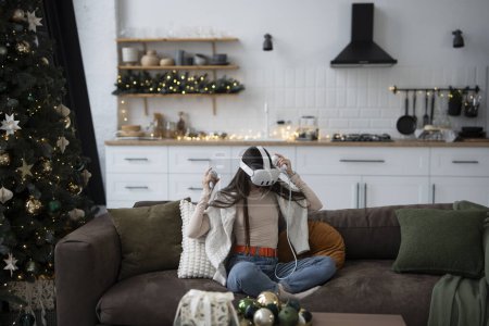 Foto de Una mujer joven con estilo en un ambiente acogedor de Navidad en casa, con un auricular de realidad virtual. Foto de alta calidad - Imagen libre de derechos