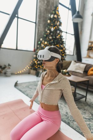 Foto de Utilizando un auricular de realidad virtual, el entrenador de yoga lleva a cabo sesiones en línea en medio de las vacaciones de Año Nuevo. Foto de alta calidad - Imagen libre de derechos