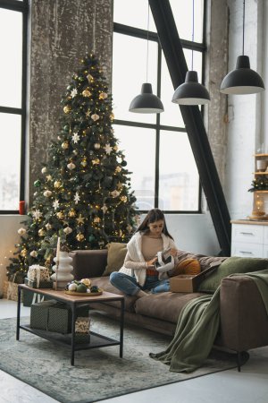 Foto de En medio de un cálido ambiente navideño en su casa, una mujer joven y elegante se ve en un auricular de realidad virtual. Foto de alta calidad - Imagen libre de derechos