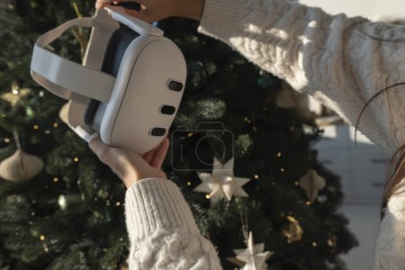 Photo for In front of a Christmas tree, a girl is holding a virtual reality headset. High quality photo - Royalty Free Image