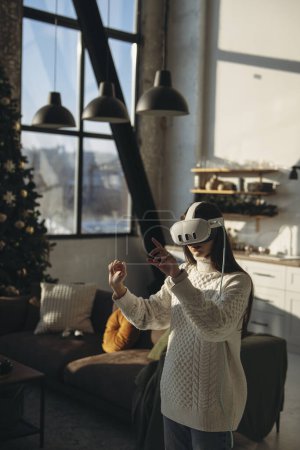 Photo for Using a virtual reality headset, a lovely young woman engages in an online game in her apartment. High quality photo - Royalty Free Image