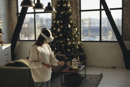 Photo for A stunning young woman plays an online game using a virtual reality headset in her apartment. High quality photo - Royalty Free Image