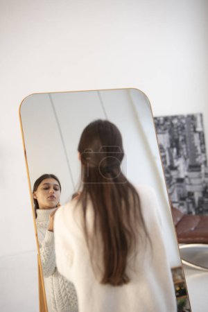 Photo for In a festive Christmas ambiance, a beautiful young woman does her makeup by the mirror. High quality photo - Royalty Free Image