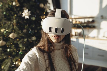 Photo for An image of a lovely girl wearing a virtual reality headset against the background of a Christmas tree. High quality photo - Royalty Free Image