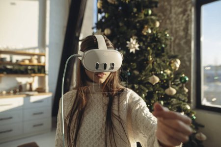 Téléchargez les photos : Un cadeau de Noël pour une jeune femme enthousiaste était un casque de réalité virtuelle. Photo de haute qualité - en image libre de droit