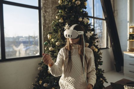 Foto de Un retrato cautivador de una chica adornada con auriculares VR, enmarcada por un árbol de Navidad. Foto de alta calidad - Imagen libre de derechos
